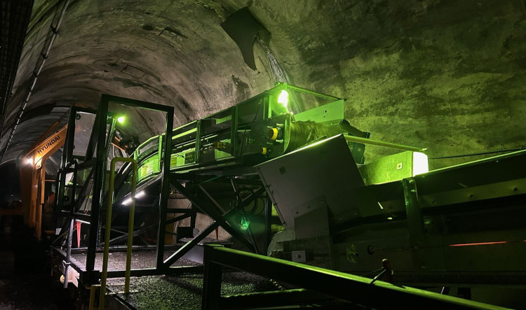 Close-up of conveyor system moving rail ballast inside a tunnel