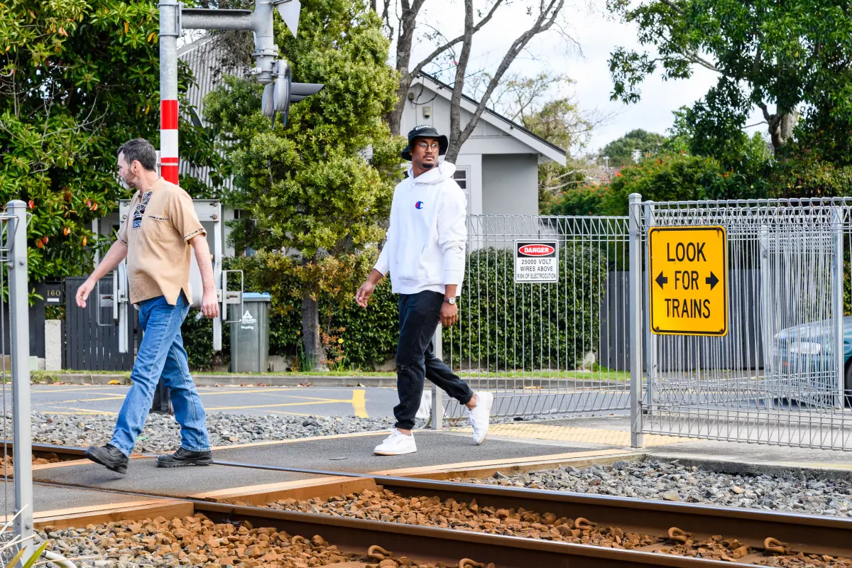 Two men walk through a level crossing looking left and right