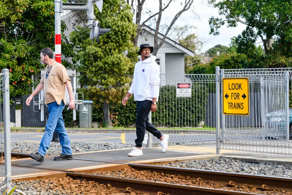 Two men walk through a level crossing looking left and right